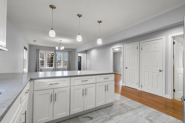 kitchen featuring white cabinetry, a notable chandelier, light wood-type flooring, hanging light fixtures, and light stone counters