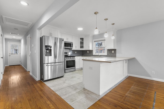 kitchen with kitchen peninsula, stainless steel appliances, backsplash, white cabinets, and sink