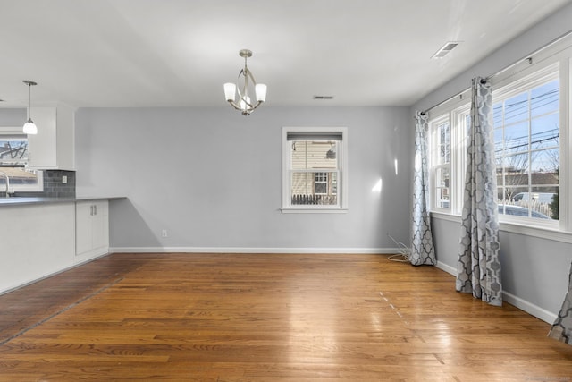 unfurnished dining area with sink, an inviting chandelier, and hardwood / wood-style floors