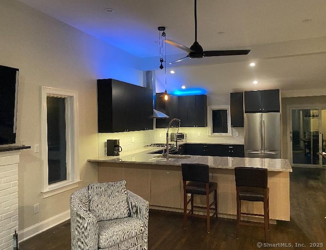 kitchen with tasteful backsplash, kitchen peninsula, stainless steel refrigerator, dark wood-type flooring, and a breakfast bar area