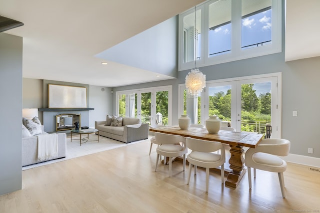 dining space with a high ceiling, an inviting chandelier, light hardwood / wood-style flooring, and french doors