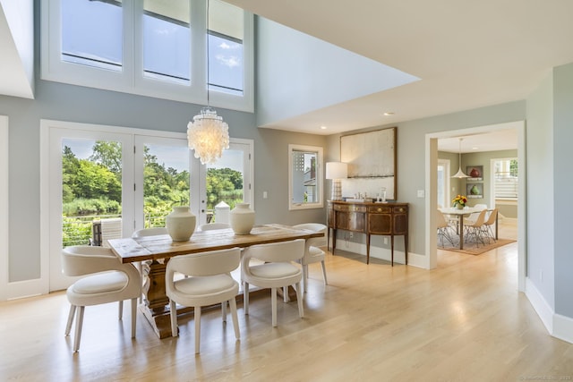 dining area featuring french doors, a towering ceiling, an inviting chandelier, and light hardwood / wood-style floors