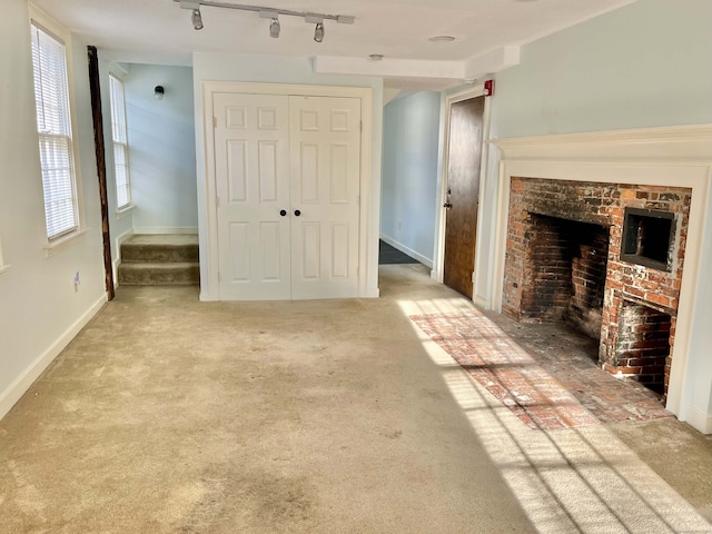 unfurnished living room featuring light colored carpet, track lighting, and a fireplace