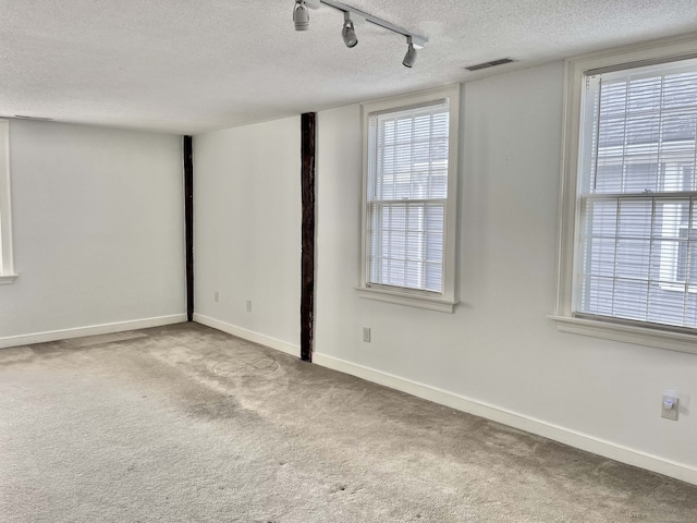 carpeted spare room with a textured ceiling and rail lighting