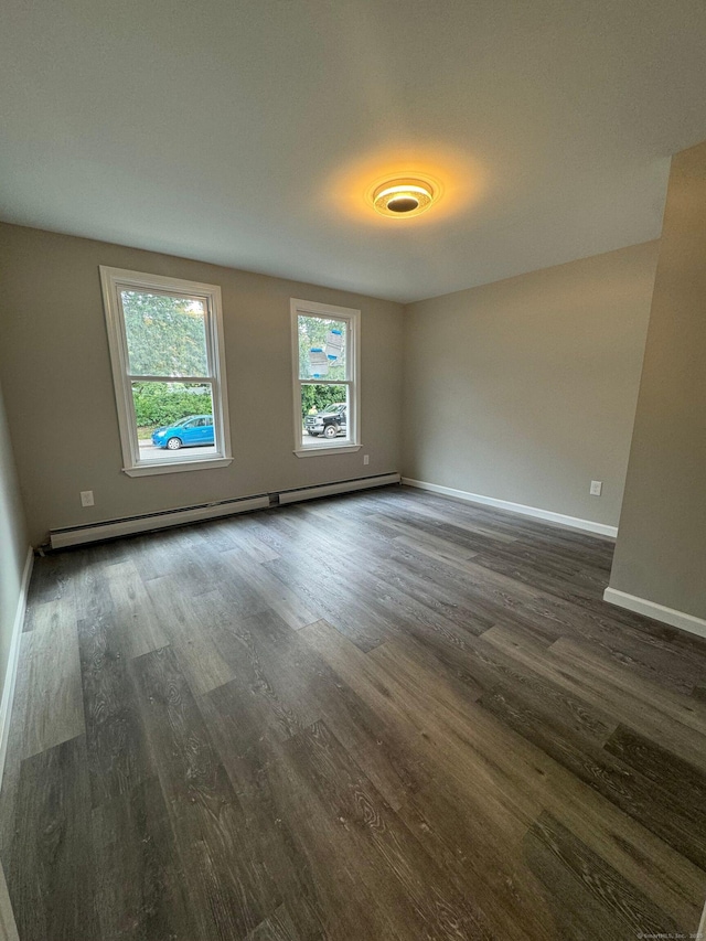 unfurnished room featuring a baseboard heating unit, baseboards, and dark wood finished floors