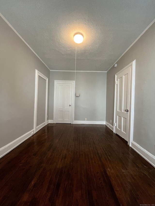 spare room with crown molding, a textured ceiling, dark wood-type flooring, and baseboards