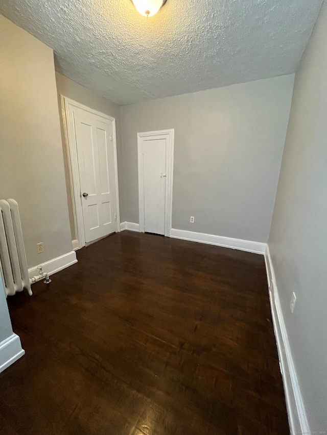 empty room with radiator, wood finished floors, baseboards, and a textured ceiling