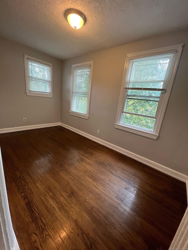 spare room with dark wood finished floors, baseboards, and a wealth of natural light