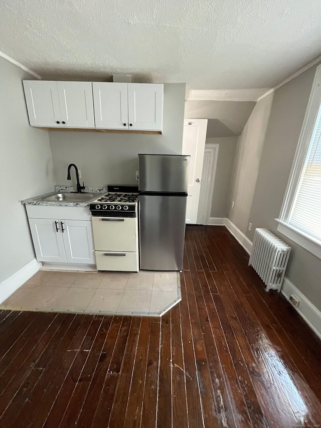 kitchen featuring white range with gas cooktop, hardwood / wood-style flooring, radiator heating unit, white cabinetry, and freestanding refrigerator