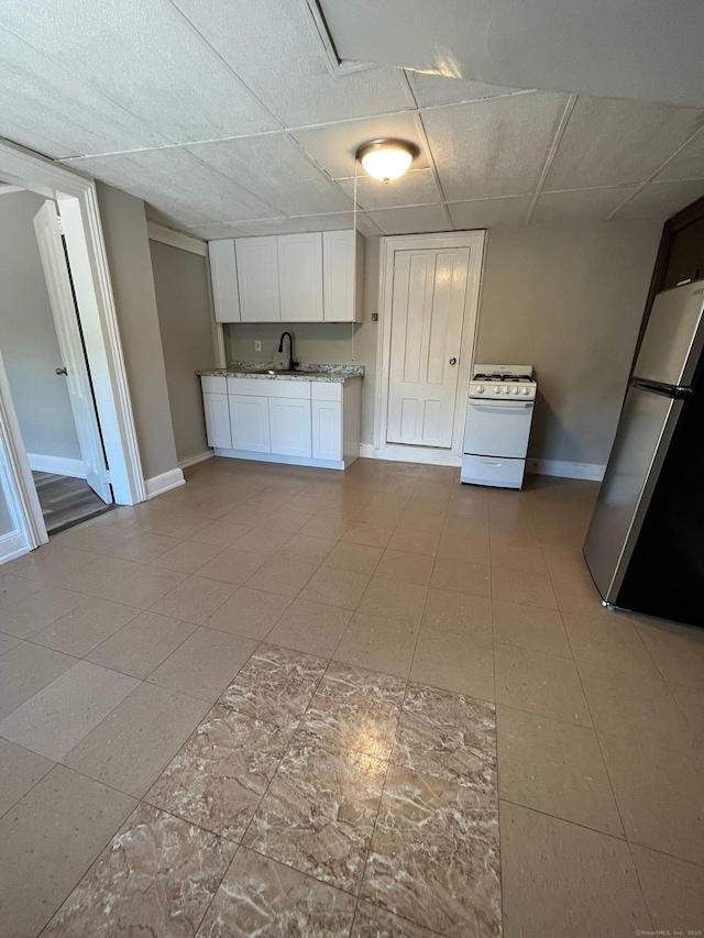 kitchen featuring white range with gas cooktop, freestanding refrigerator, a sink, a paneled ceiling, and white cabinetry