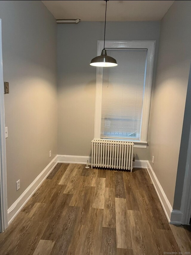 unfurnished dining area featuring radiator heating unit, wood finished floors, and baseboards