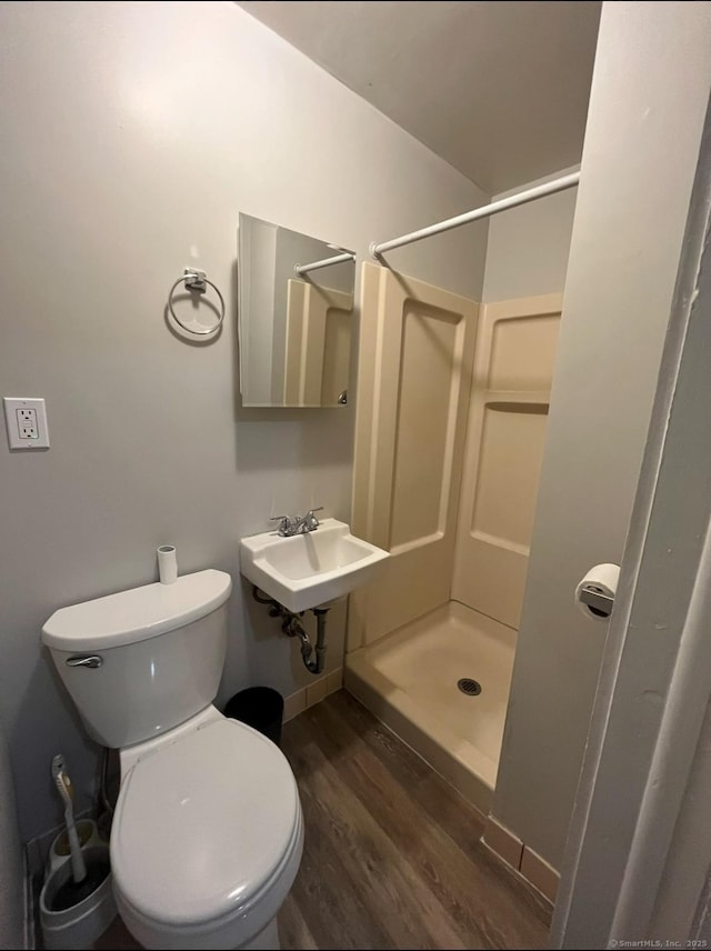 bathroom featuring toilet, a stall shower, a sink, wood finished floors, and baseboards