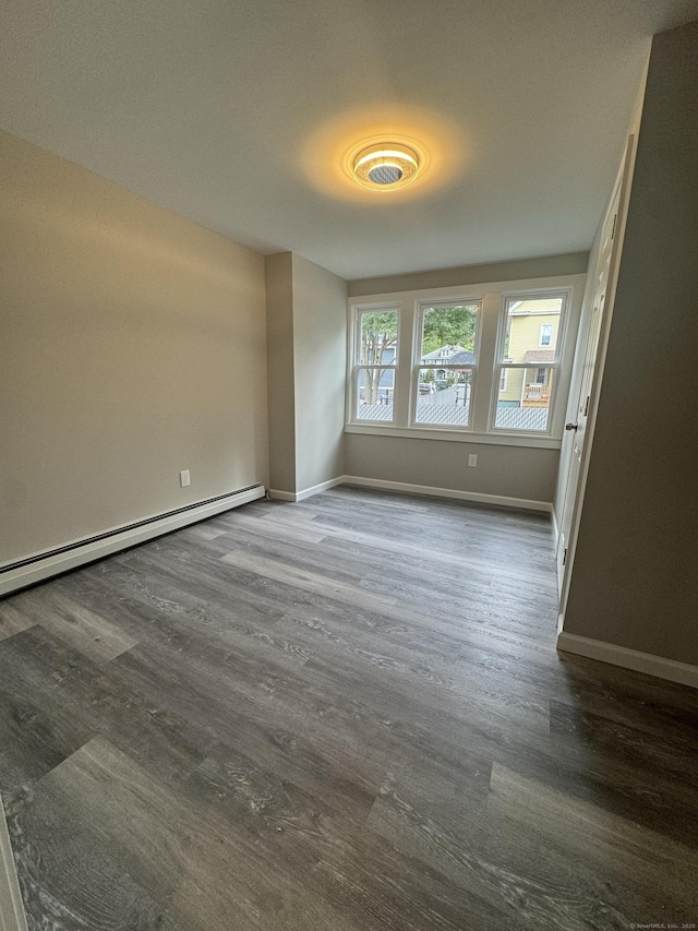 empty room featuring a baseboard heating unit, dark wood finished floors, and baseboards