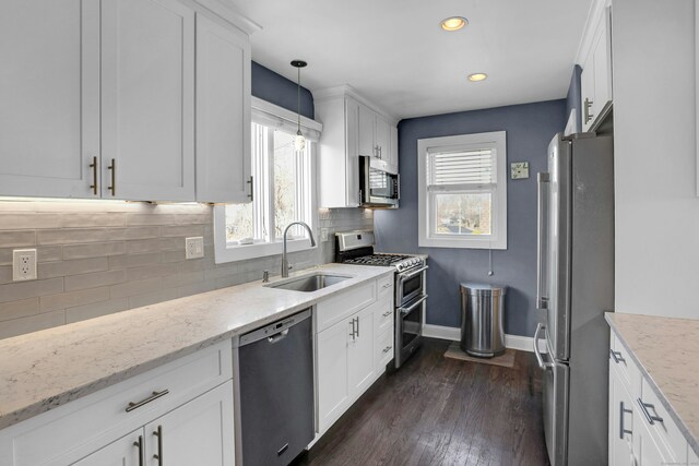 kitchen with sink, stainless steel appliances, light stone countertops, white cabinets, and decorative light fixtures