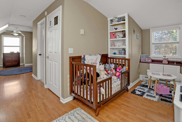 bedroom with multiple windows, lofted ceiling, a crib, and light hardwood / wood-style flooring