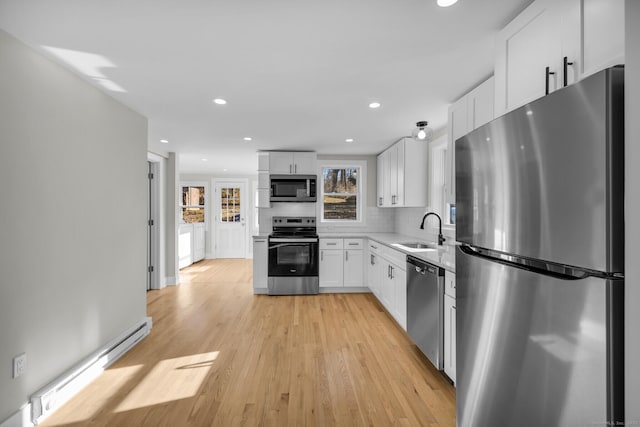 kitchen with a baseboard heating unit, stainless steel appliances, light wood-type flooring, white cabinets, and sink