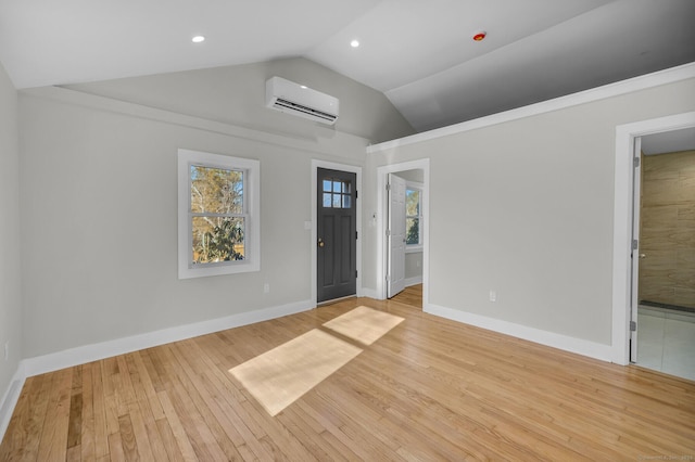 empty room with lofted ceiling, a wall mounted AC, and light wood-type flooring