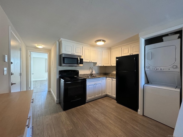 kitchen with black appliances, stacked washer / drying machine, white cabinetry, and hardwood / wood-style flooring