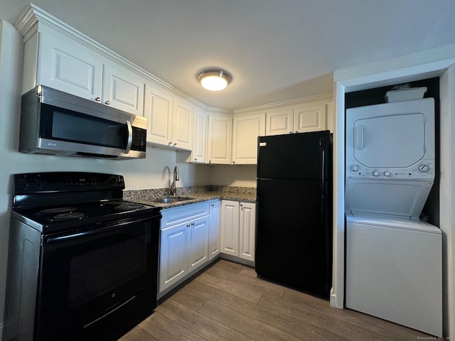 kitchen featuring light hardwood / wood-style floors, black appliances, sink, white cabinetry, and stacked washer and dryer