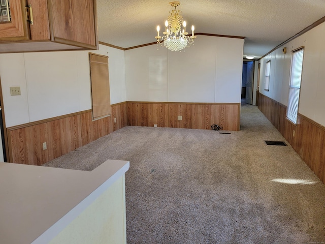 empty room with a notable chandelier, carpet flooring, a textured ceiling, and ornamental molding