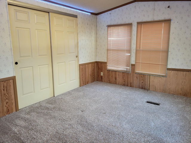 unfurnished bedroom with a closet, ornamental molding, lofted ceiling, and carpet flooring