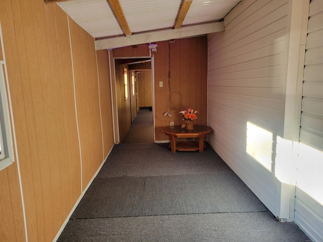 corridor featuring beam ceiling, carpet, and wooden walls