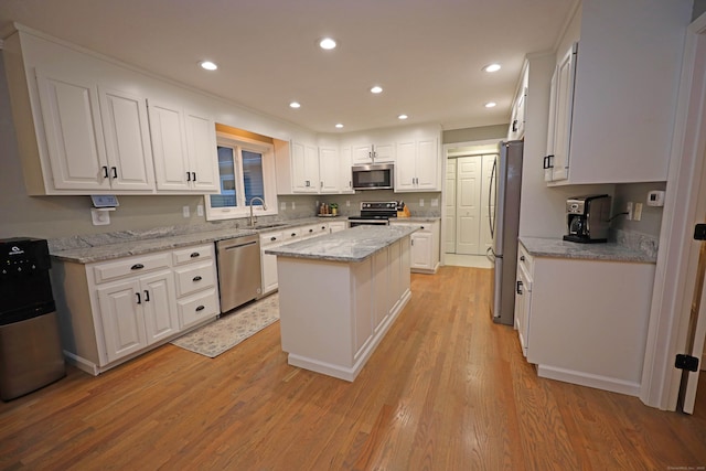 kitchen with light stone counters, white cabinetry, a center island, and stainless steel appliances