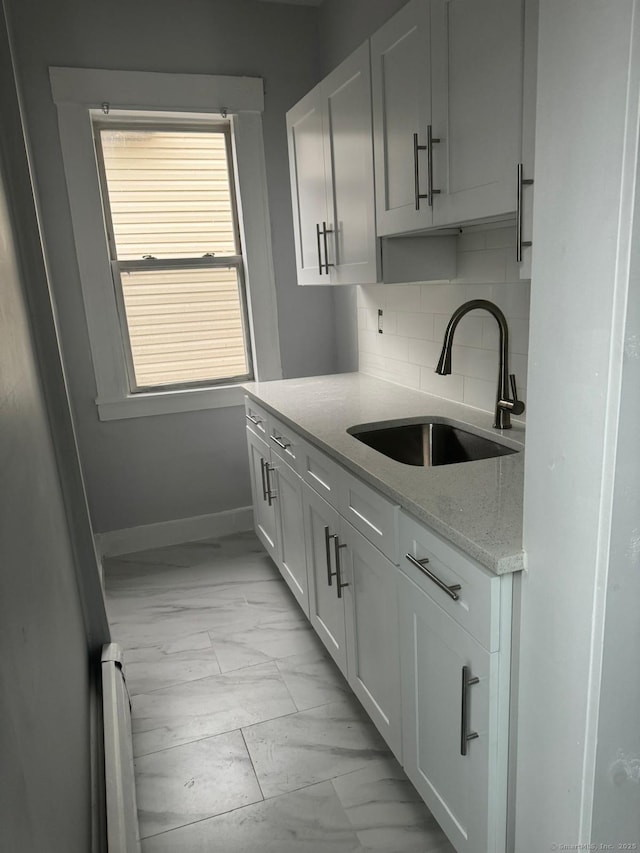 kitchen featuring sink, white cabinetry, light stone counters, and decorative backsplash