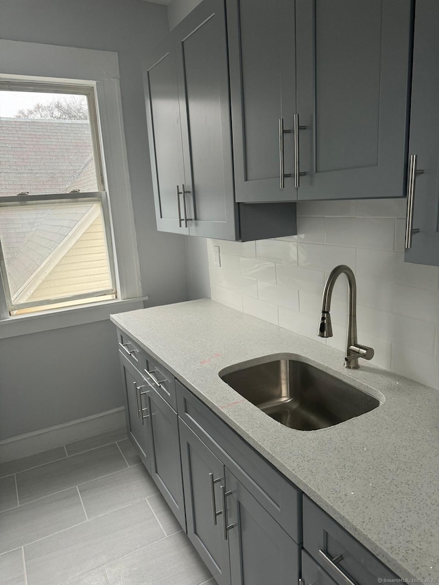 kitchen featuring sink, decorative backsplash, gray cabinetry, and light stone counters