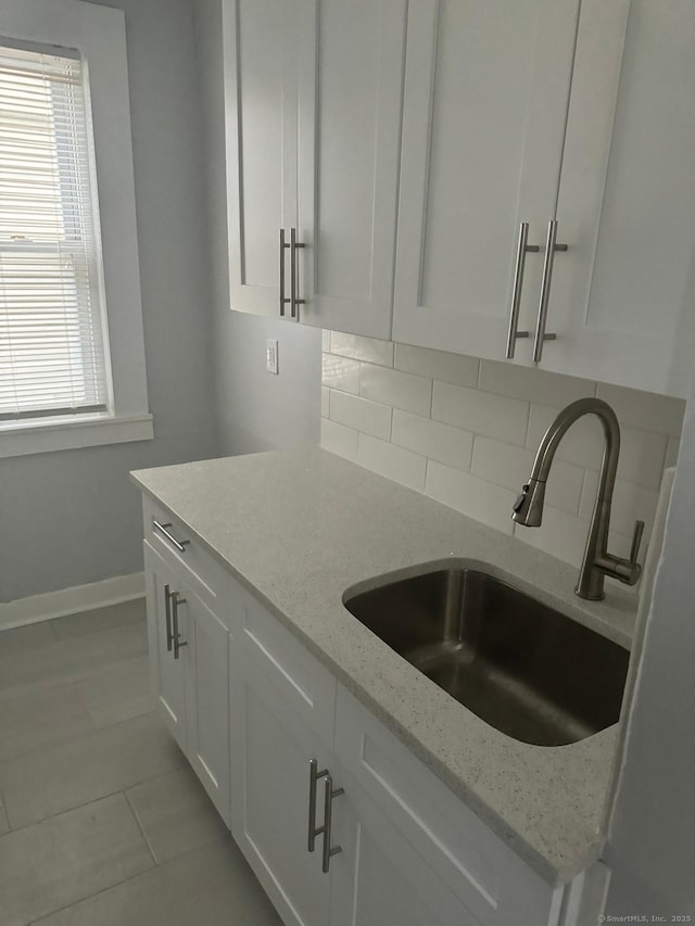 kitchen featuring sink, backsplash, white cabinetry, and light stone countertops