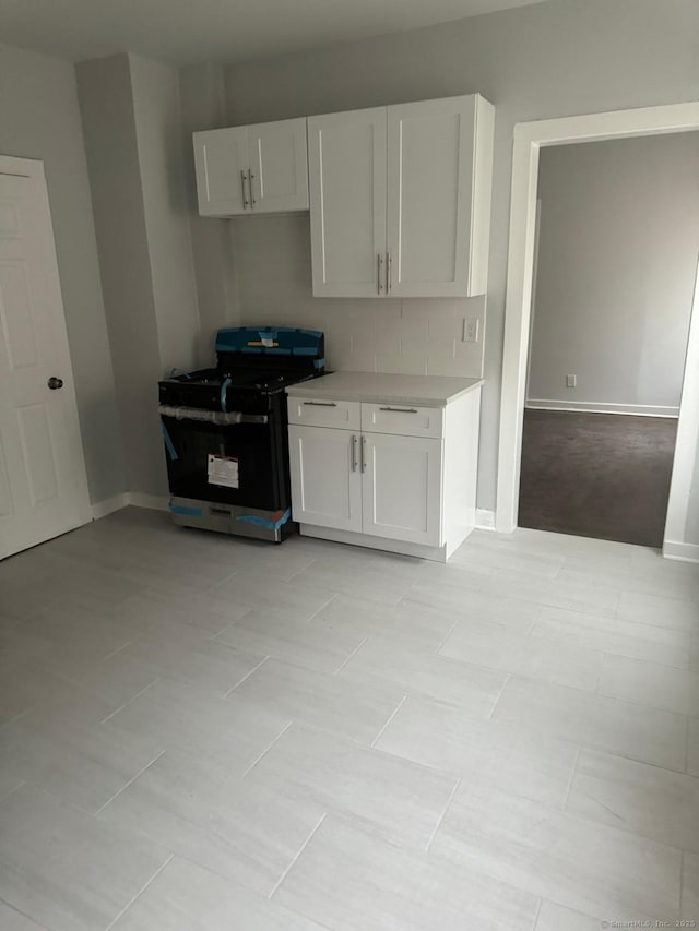 kitchen featuring stove, white cabinets, decorative backsplash, and light tile patterned floors