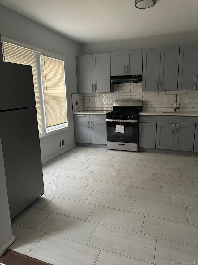 kitchen featuring stainless steel range with gas stovetop, black fridge, gray cabinets, and sink