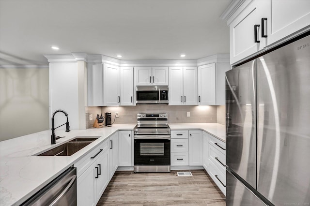 kitchen with appliances with stainless steel finishes, backsplash, light stone countertops, white cabinets, and sink