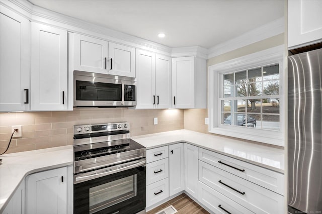 kitchen with white cabinets, backsplash, appliances with stainless steel finishes, and light hardwood / wood-style flooring