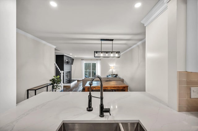 kitchen featuring pendant lighting, wood-type flooring, sink, crown molding, and light stone countertops