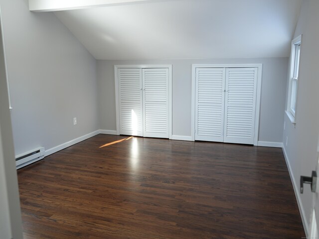 unfurnished bedroom featuring a baseboard radiator, two closets, lofted ceiling, and dark hardwood / wood-style flooring