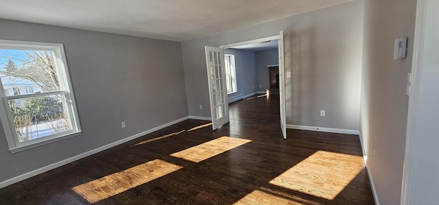 empty room featuring a fireplace, a baseboard radiator, and dark hardwood / wood-style flooring