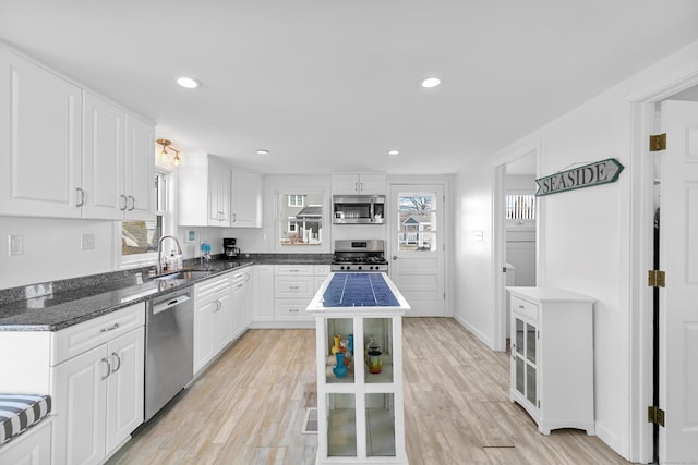 kitchen with white cabinetry, appliances with stainless steel finishes, light wood-type flooring, a kitchen island, and sink