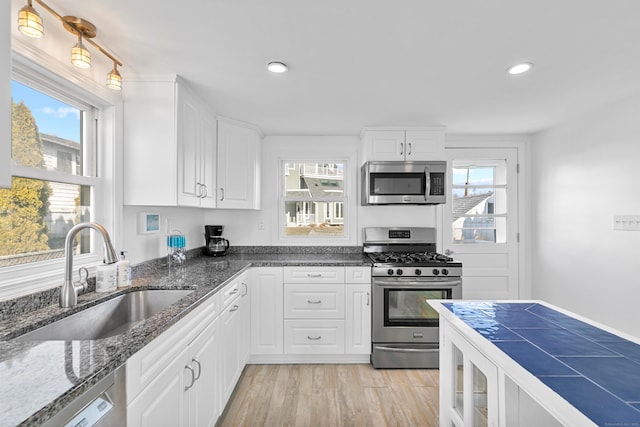 kitchen with appliances with stainless steel finishes, white cabinetry, dark stone countertops, sink, and light wood-type flooring