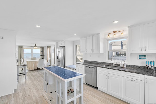 kitchen featuring white cabinetry, light hardwood / wood-style floors, appliances with stainless steel finishes, dark stone counters, and sink