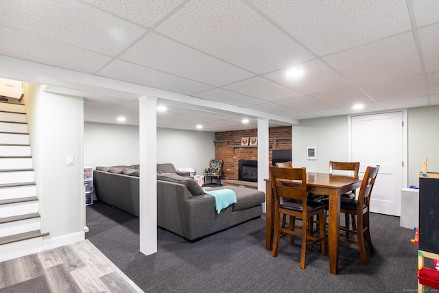 dining area featuring a brick fireplace, a drop ceiling, and dark hardwood / wood-style flooring