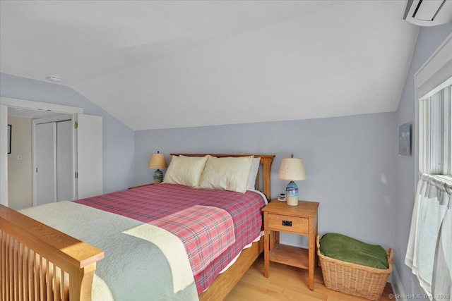 bedroom with lofted ceiling, a wall mounted AC, and light hardwood / wood-style floors