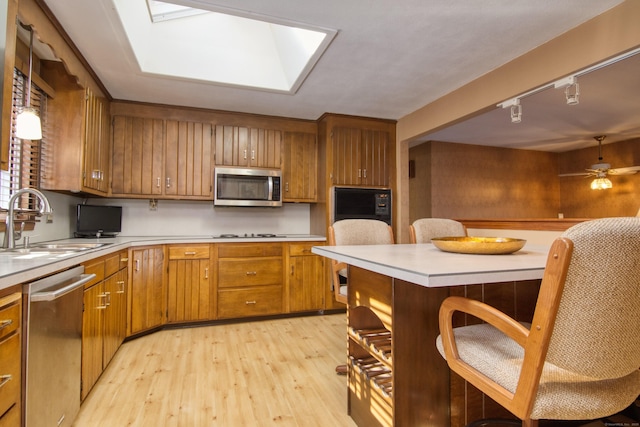 kitchen with rail lighting, sink, ceiling fan, stainless steel appliances, and light hardwood / wood-style flooring