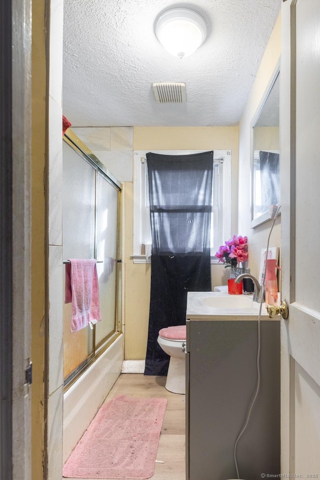 full bathroom with toilet, shower / bath combination with glass door, a textured ceiling, vanity, and hardwood / wood-style flooring