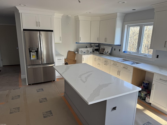 kitchen with light stone counters, stainless steel fridge, a kitchen island, and white cabinetry