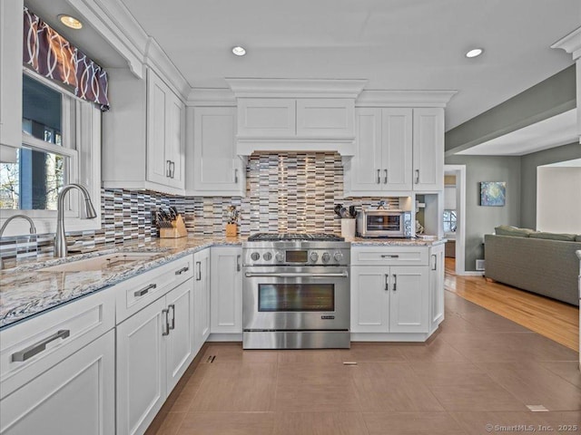 kitchen featuring decorative backsplash, sink, white cabinetry, and high end stove