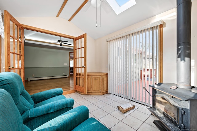 tiled living room featuring ceiling fan, a wood stove, a baseboard radiator, and lofted ceiling with skylight