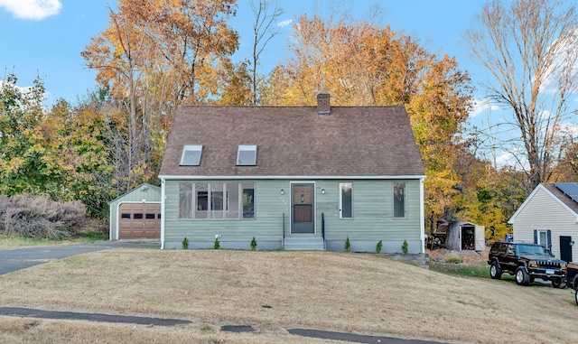 cape cod-style house with a garage, a front yard, and an outbuilding