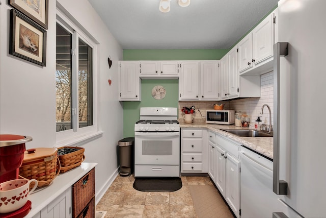 kitchen with sink, white cabinets, decorative backsplash, light stone countertops, and white appliances