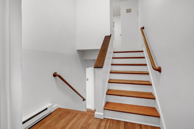 staircase featuring a baseboard heating unit and hardwood / wood-style flooring